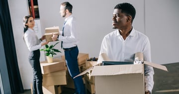 Three young office workers moving packed boxes in office